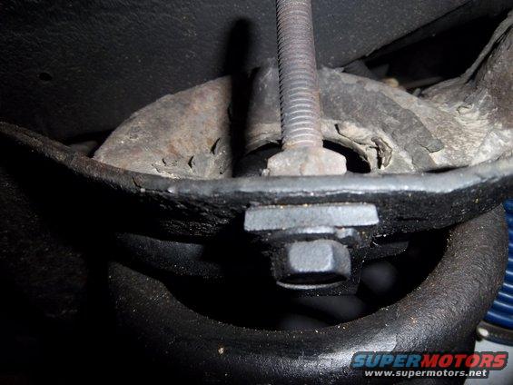 Close-up of a rusty metal suspension part with a large bolt going through it. A blue spring is visible in the background