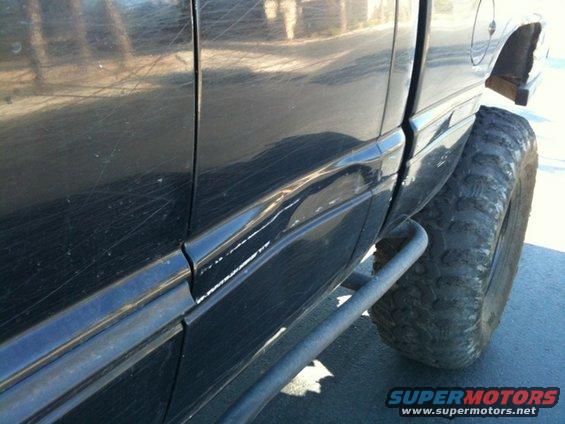 Black pickup truck side panel with dents and scratches, large off-road tire visible