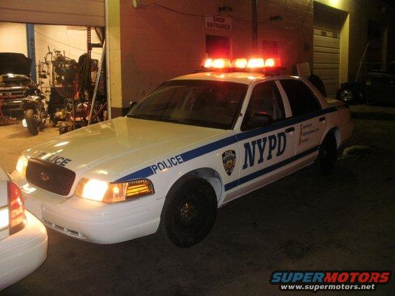 White 2002 Ford Crown Victoria police car with NYPD markings and emergency lights on