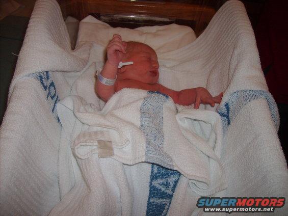 Newborn baby wrapped in white towels, wearing a hospital bracelet