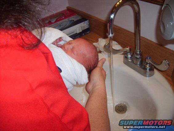 Baby being bathed in a sink with running water