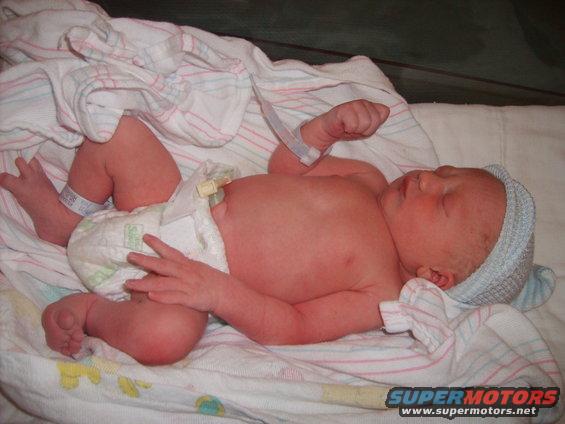 Newborn baby wearing a blue cap and diaper, lying on a blanket