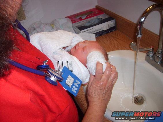 Nurse bathing a newborn baby in a sink with a stethoscope around her neck