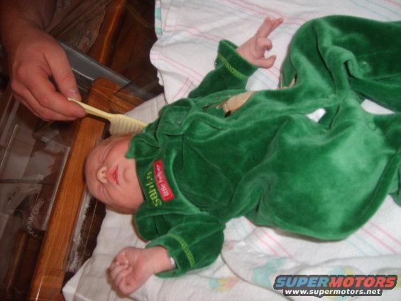 Baby in green outfit getting hair brushed by an adult's hand