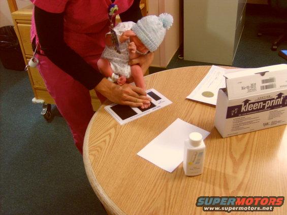 Newborn baby's foot being inked on a card with a bottle of powder and a box of Kleen-Print nearby