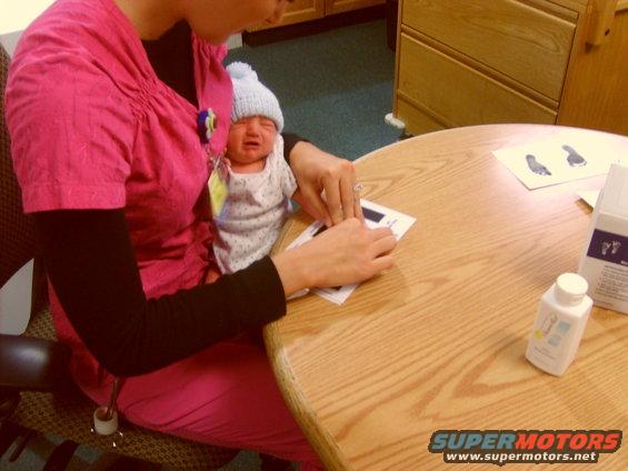 Crying baby in a blue hat held by a person in a pink shirt