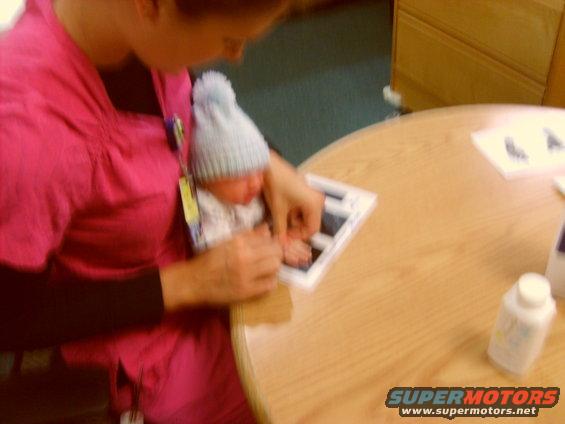 Person in pink scrubs holding a baby wearing a blue hat, looking at a picture frame