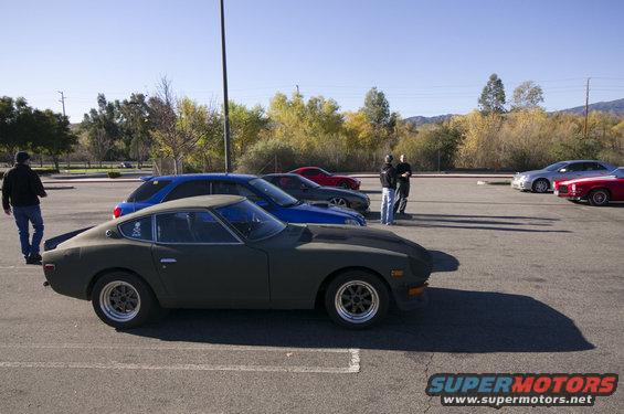 Dark green coupe, 3/4 front view, parked in a lot with other cars