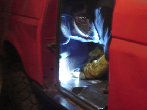 Welding sparks fly inside a red vehicle's interior, near the door frame