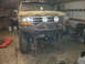 1995 Ford Bronco - A camouflaged Ford Bronco is elevated on jack stands in a garage, showing its front end and custom modifications.
