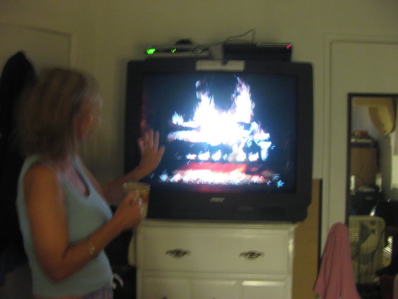 Woman holding a cup watches a television displaying a fireplace scene