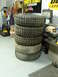 1971 International School Bus - A stack of five large off-road tires sits in a garage, with tools and equipment in the background.