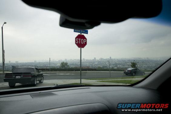 View from inside a car looking out at two other cars on a road, with a city skyline in the distance