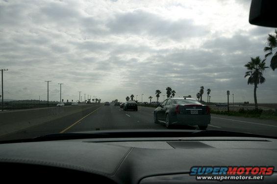 Car driving on highway with palm trees and cloudy sky. Other cars on the road