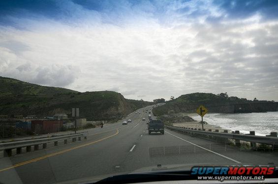 Dark SUV driving on a highway next to the ocean