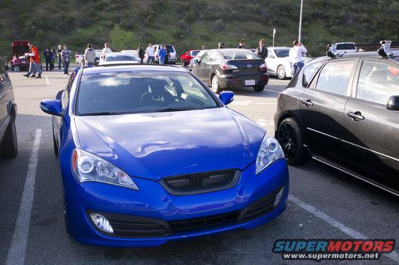 Blue coupe parked in lot, black car next to it. People in background