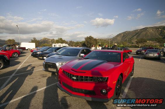 Red Chevrolet Camaro SS with black stripes parked in a lot with other cars. Mountains in background
