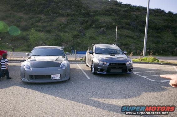 Two sports cars, a gray Nissan 350Z and a dark gray Mitsubishi Lancer Evolution, are parked side-by-side in a lot