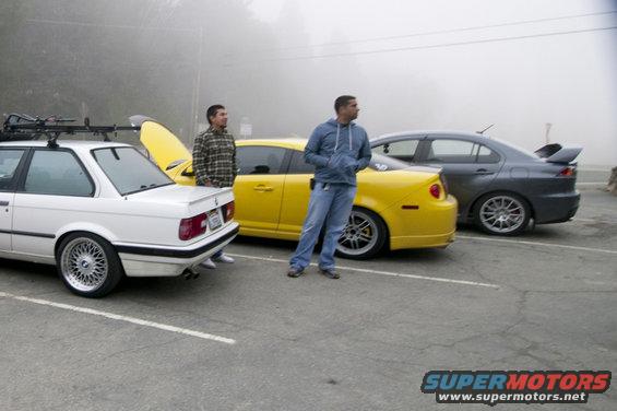 White BMW, yellow car, and gray sedan parked in a lot with two guys standing around