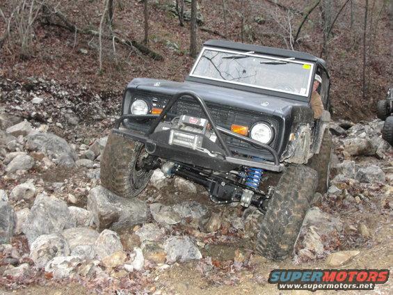 Black Ford Bronco with winch on front bumper navigating a rock-strewn trail. Another vehicle is partially visible to the right