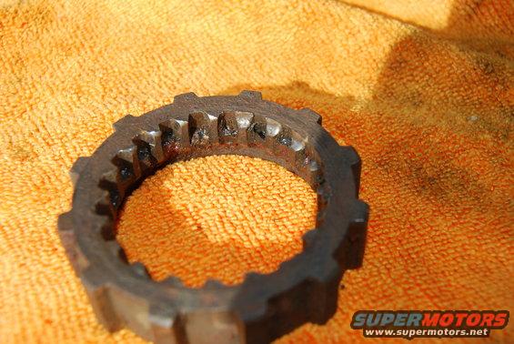 Close-up of a rusty, toothed metal ring with worn teeth, resting on an orange textured cloth