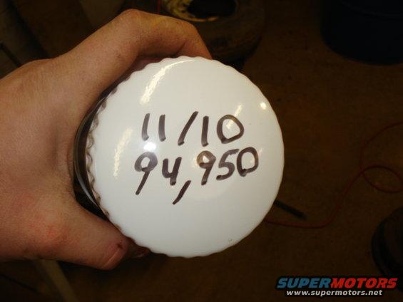 Hand holding a white oil filter with '11/10' and '94,950' written on it