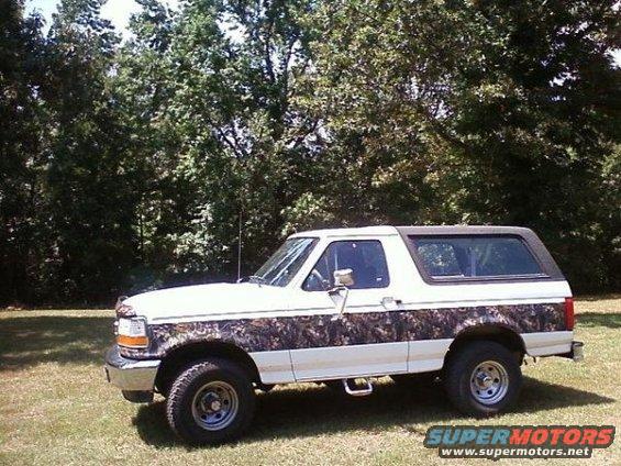 White Ford Bronco with camouflage body panels parked on grass