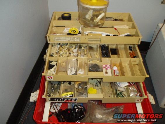 Tan multi-drawer tool chest filled with small parts and supplies, sitting in a red plastic toolbox
