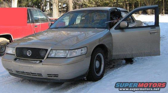 Gold Mercury Grand Marquis with driver's door open, parked in snow next to a red truck