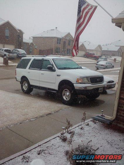 White 2002 Ford Expedition parked on a snowy street with an American flag flying
