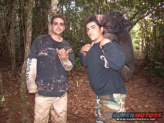 Two men in a wooded area, one carrying a large wild boar over his shoulders