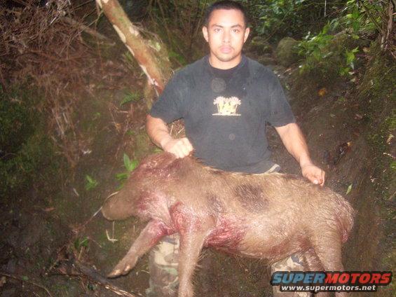Man with a dead wild boar in a wooded area. Watermark reads SUPERMOTORS.NET