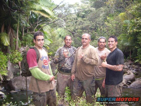 Five men stand in a jungle near a stream, some holding fishing rods