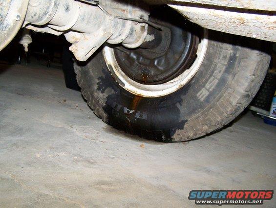 Undercarriage of a vehicle showing a tire with fluid leaking onto the concrete floor