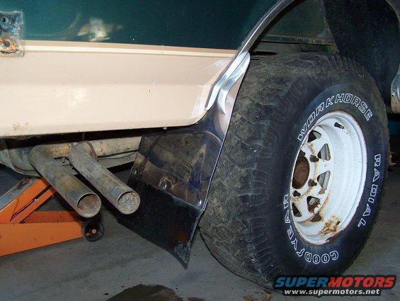 Close-up of a vehicle's rear tire and dual exhaust pipes. The tire is a Goodyear Workhorse Radial. The body is two-tone green and tan