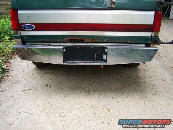 Rear of a green Ford pickup with a chrome bumper and a red stripe on the tailgate. Some rust is visible
