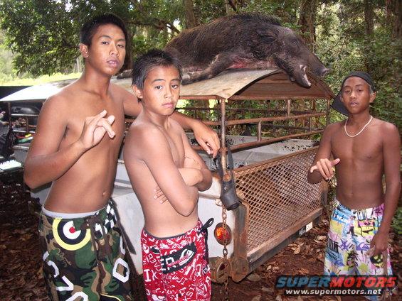 Trailer with a wild boar on top, three young men standing nearby