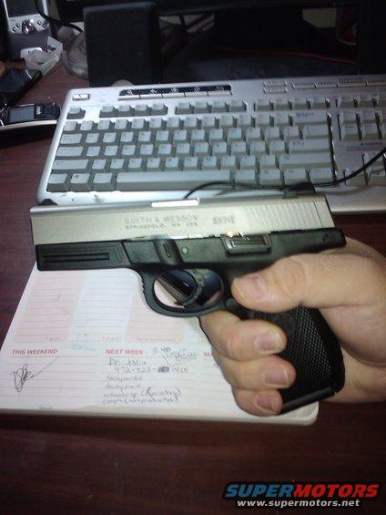 Hand holding a Smith & Wesson pistol over a notepad with writing