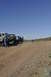 1991 Ford Bronco - Multiple off-road vehicles are parked on a dusty dirt road under a clear blue sky.