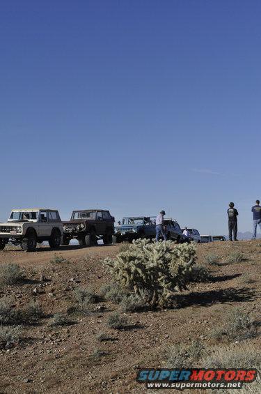 Tan 1978 Ford Bronco parked on a dirt road with other vehicles and people