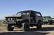 1991 Ford Bronco - A modified Ford Bronco is parked in a line with other off-road vehicles under a clear blue sky.