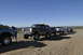 1991 Ford Bronco - A line of SUVs and trucks are parked on a dirt road under a clear blue sky.