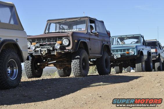 Several Ford Broncos lined up on a dirt road, one in front has a winch and off-road tires