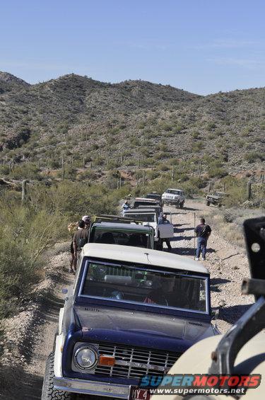 Dark blue Ford Bronco with white top, front view, on a dirt road