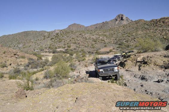 Dark SUV on rocky desert trail with other vehicles behind