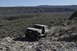 1991 Ford Bronco - A tan Ford Bronco navigates a rocky, off-road trail in a desert landscape.
