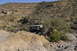 1991 Ford Bronco - A tan off-road vehicle navigates a rocky, desert landscape with sparse vegetation and cacti.