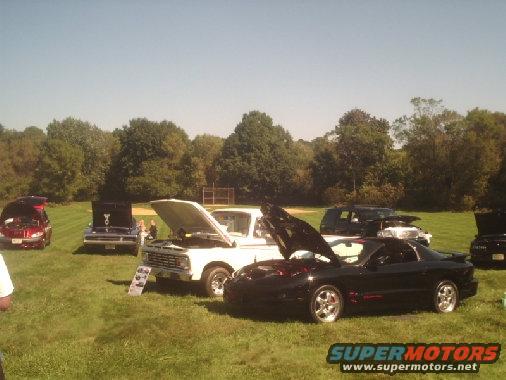 Car show with several cars and trucks on display, hoods open, on a grassy field