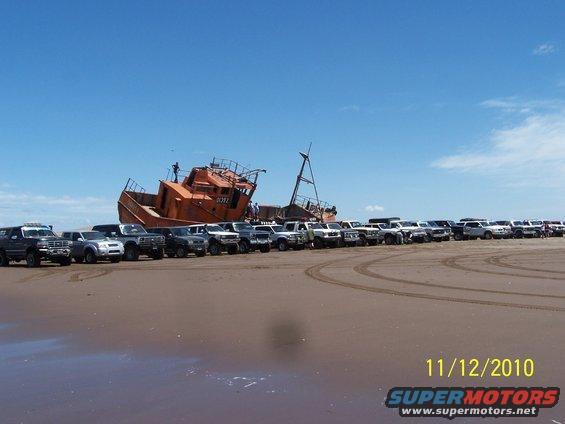 Line of SUVs and trucks parked on a beach with a shipwreck in the background. Date 11/12/2010 visible