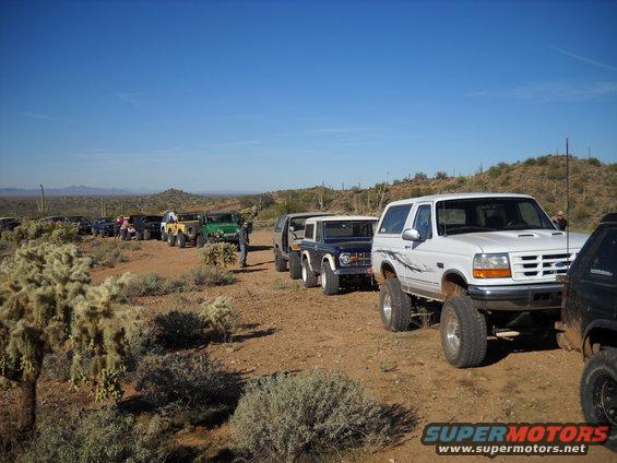 1996 Ford Bronco leading a line of off-road vehicles on a dirt road in the desert